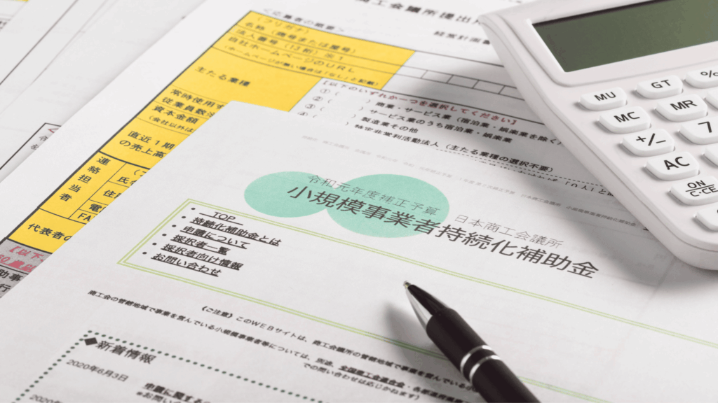小規模企業向け補助金の申請書類。黄色と緑色の枠で囲まれた記入項目と、計算機、ペンが配置されている